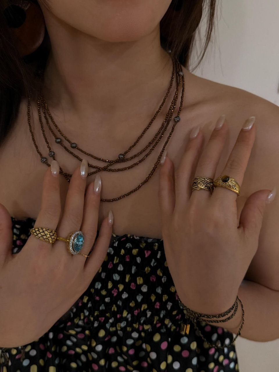 Frontal view showing multiple gold textured rings stacked on hands, layered bronze necklaces at different lengths, paired with black patterned top