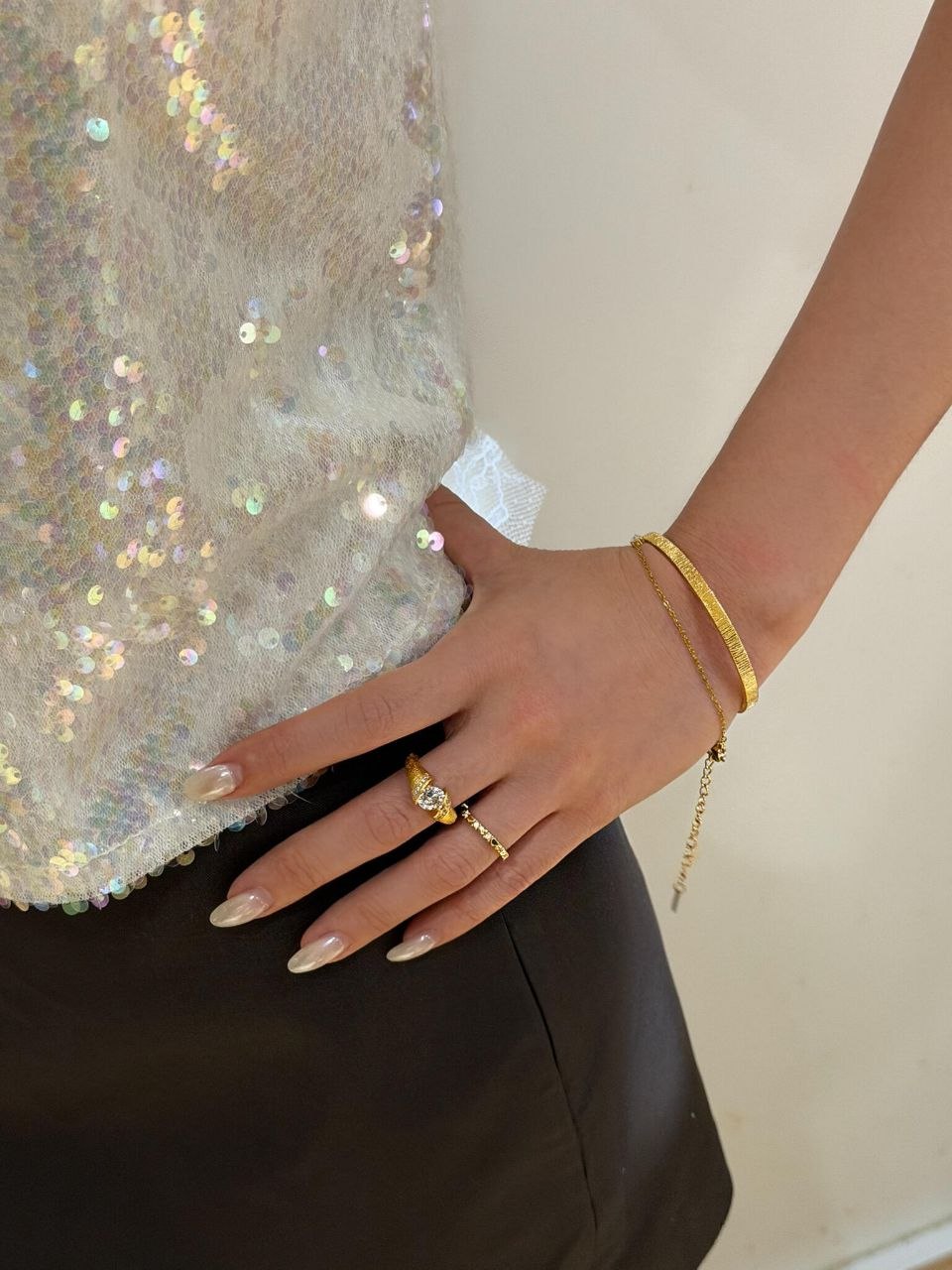 Side view of wrist showing stacked gold rings and delicate gold bracelet worn together, demonstrating minimalist layering