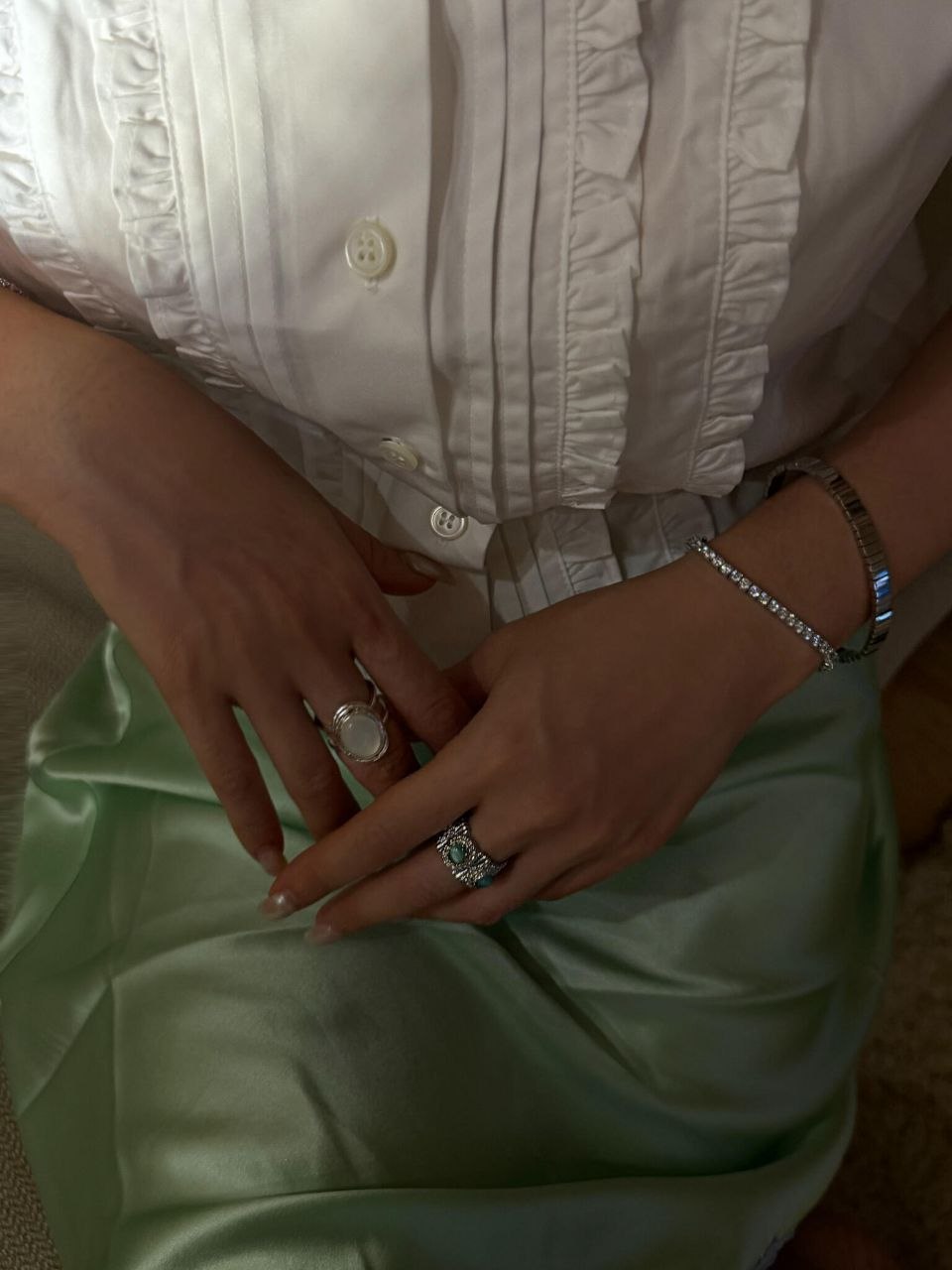 Wrist detail showing multiple silver pearl bracelets layered together with green fabric background