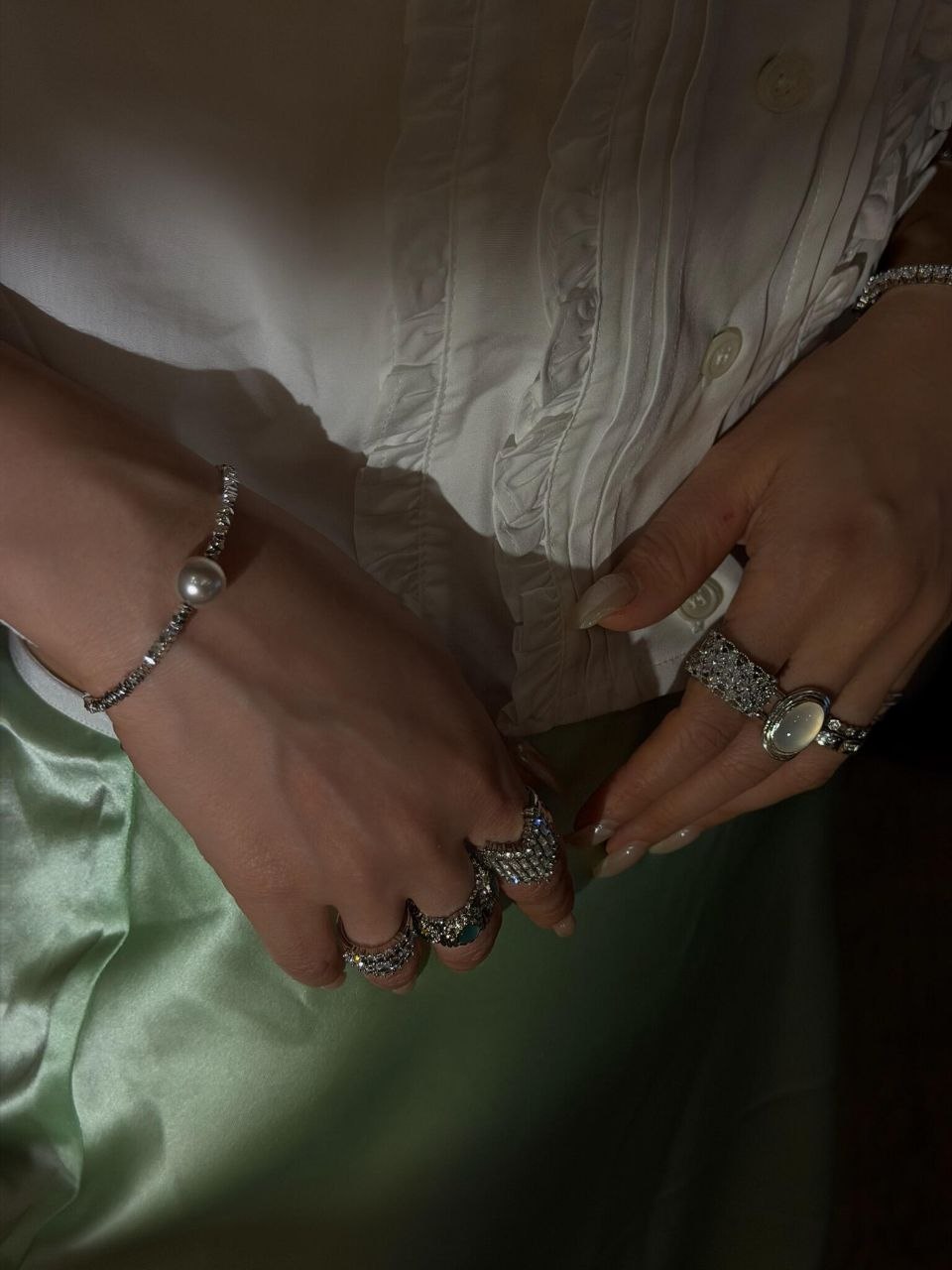 Hand detail showing multiple silver diamond rings stacked with pearl bracelets, demonstrating balanced layering