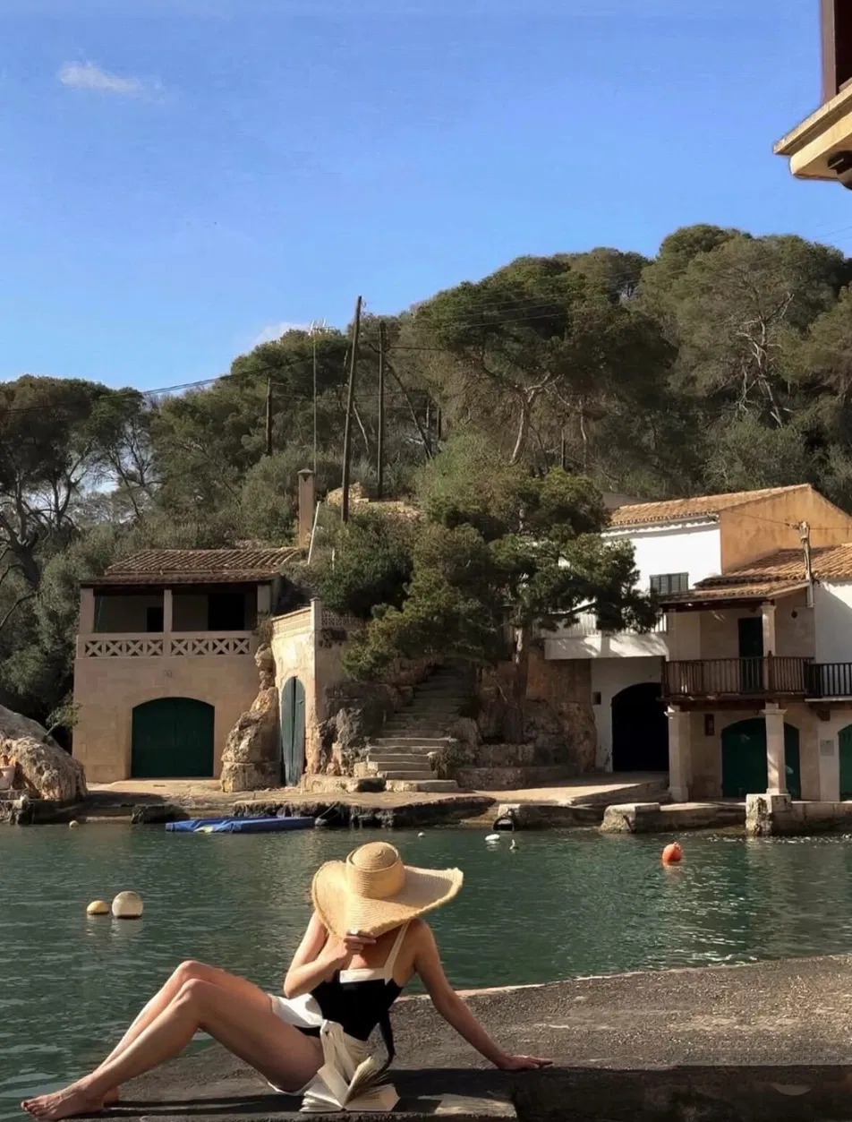 Woman in cream wide-brim hat sitting by the water at a Mediterranean-style coastal location