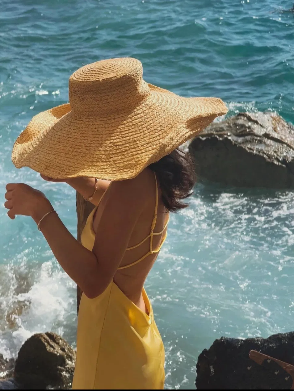 Woman in bright yellow swimsuit and oversized golden straw hat wading in clear turquoise water